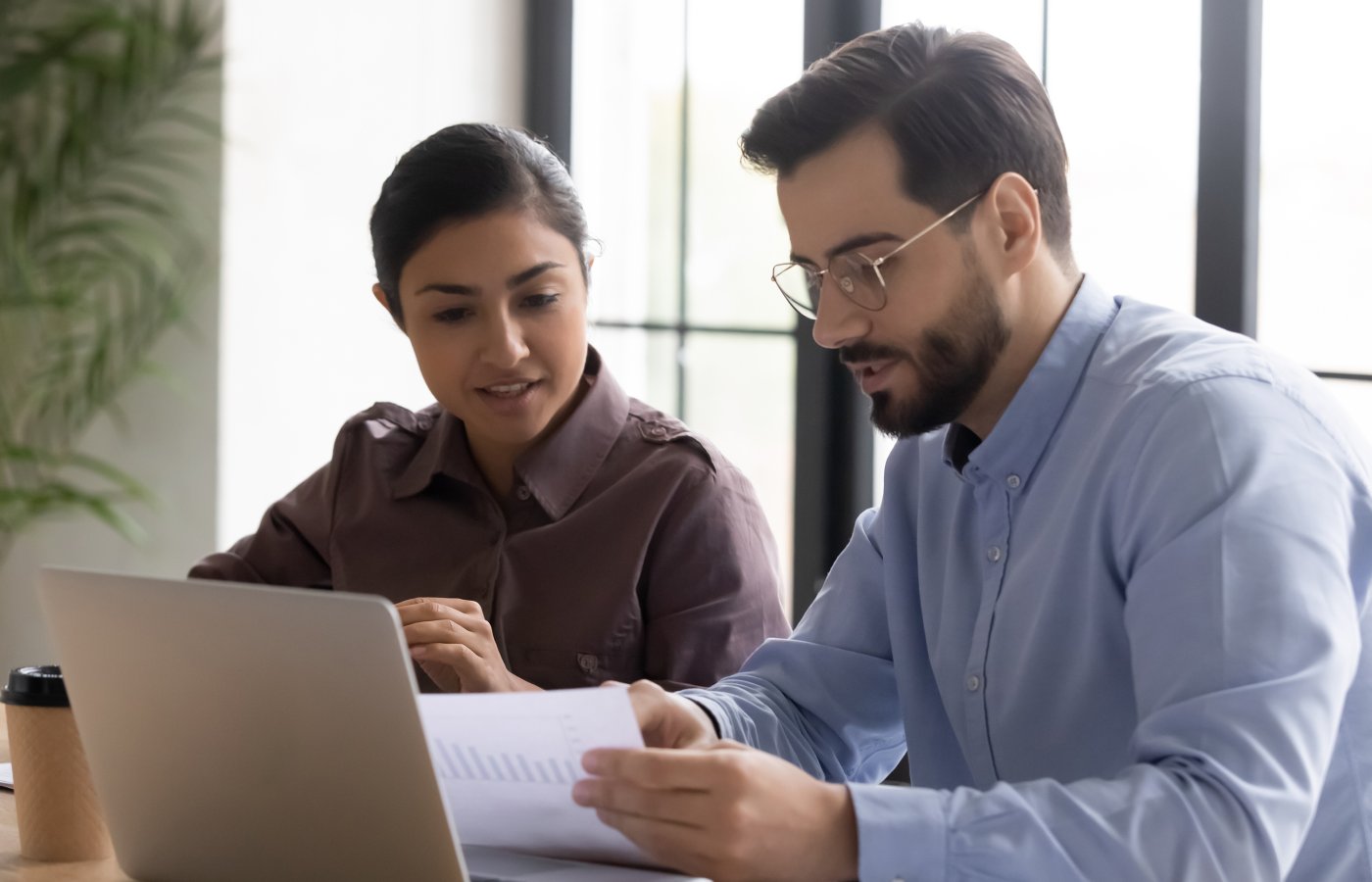 Man and woman reviewing paper in front of laptop computer. 