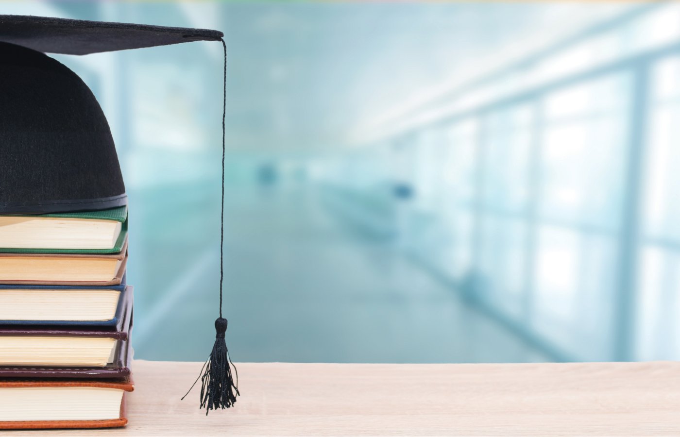 Mortarboard on top of stack of books with classroom in the background