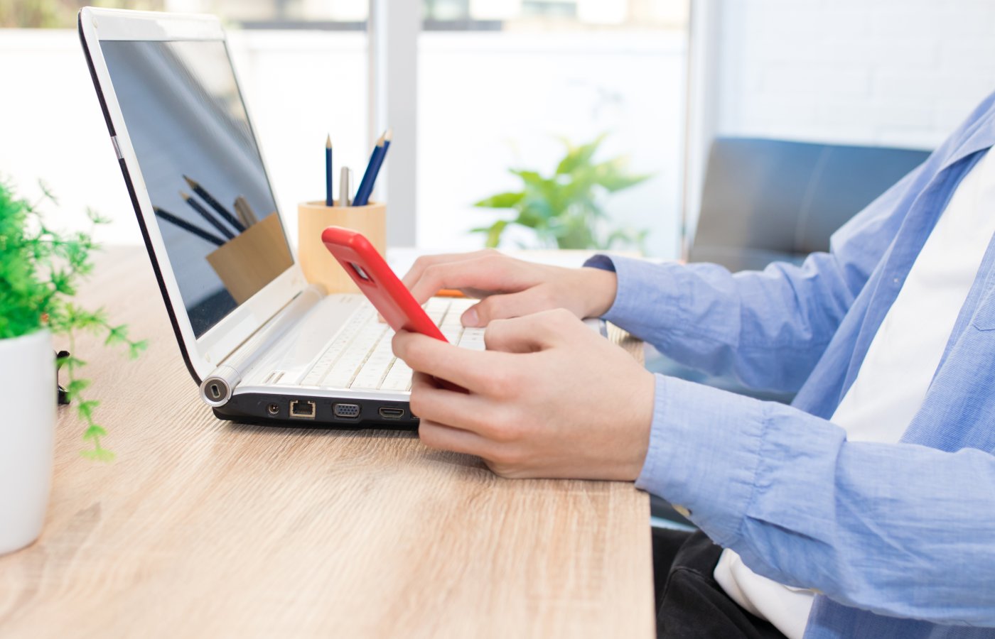 person on laptop computer while holding cell phone