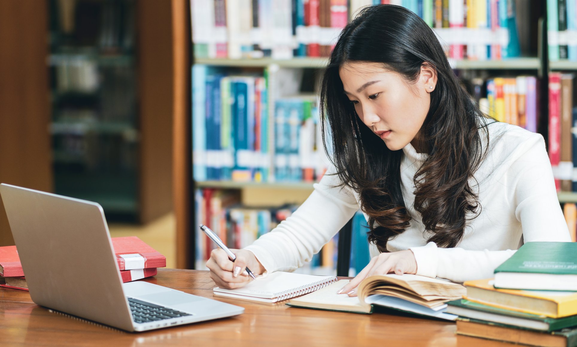 woman looking at laptop and writing in notebook 