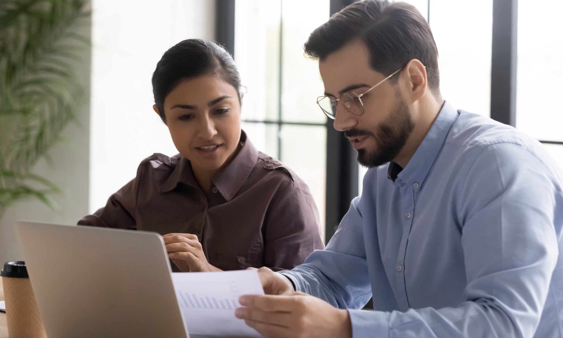 Man and woman reviewing paper in front of laptop computer. 