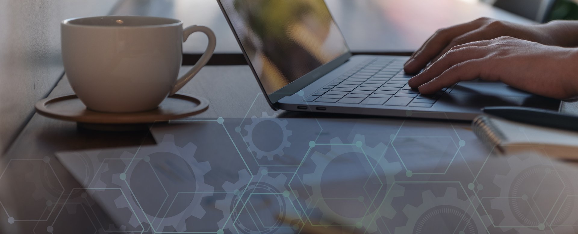 closeup of hands typing on a laptop with a cup of coffee and papers nearby. Overlay of gears icons and lines as well. 