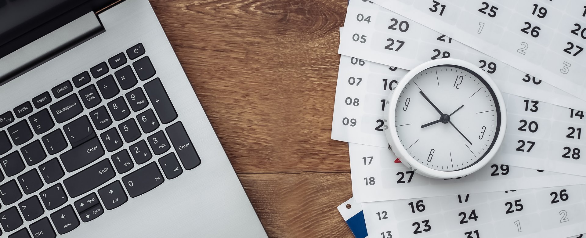 overhead view of a laptop, pages from a calendar, and a clock