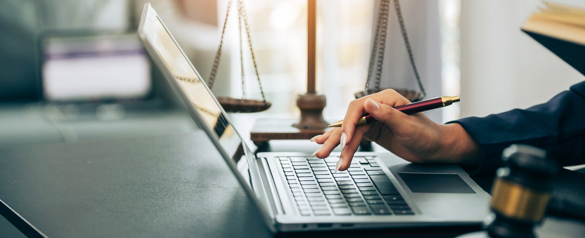 close up of hands at a laptop with a gavel and scale of justice sitting on the desk