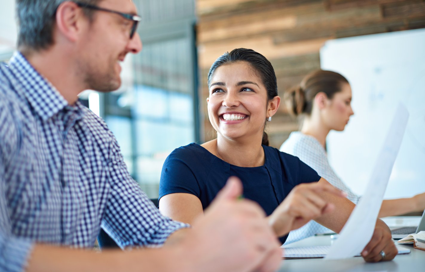 A woman and man talking in an office environment. She is holding a piece of paper and smiling