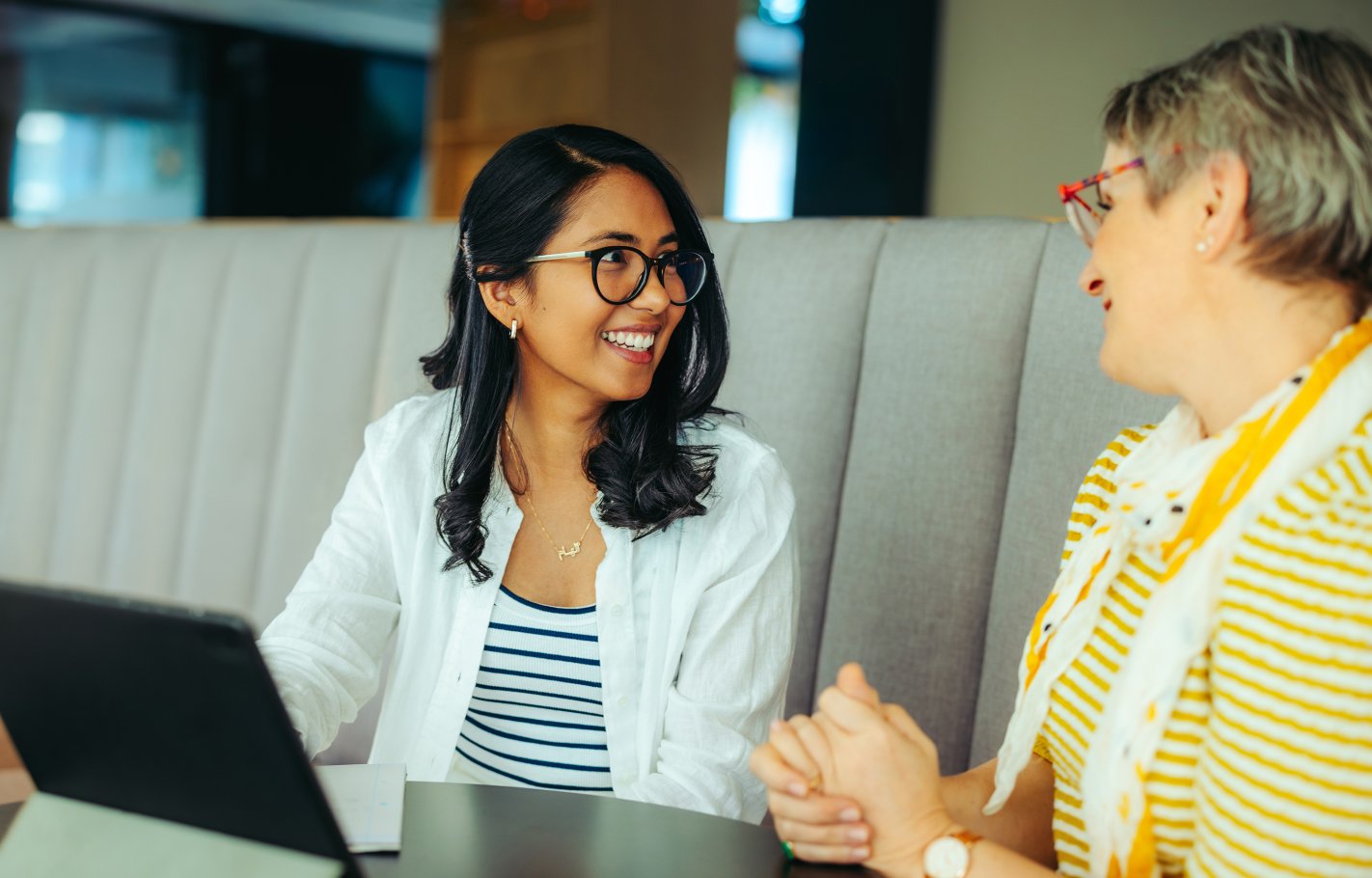 college-age woman talking with an older woman (teacher) at a table with a laptop