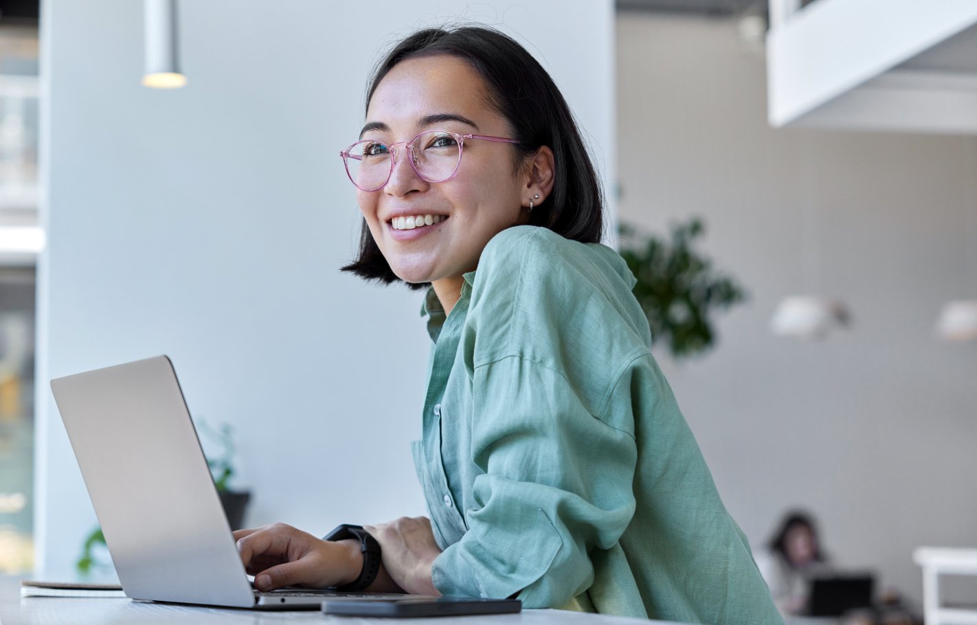 Young woman smiling while sitting at a table and working on a laptop. 
