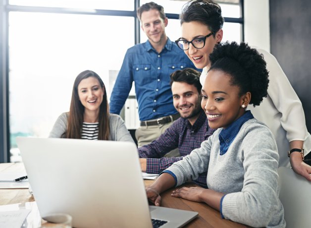 Group of young professionals in an office environment talking and looking at a laptop screen