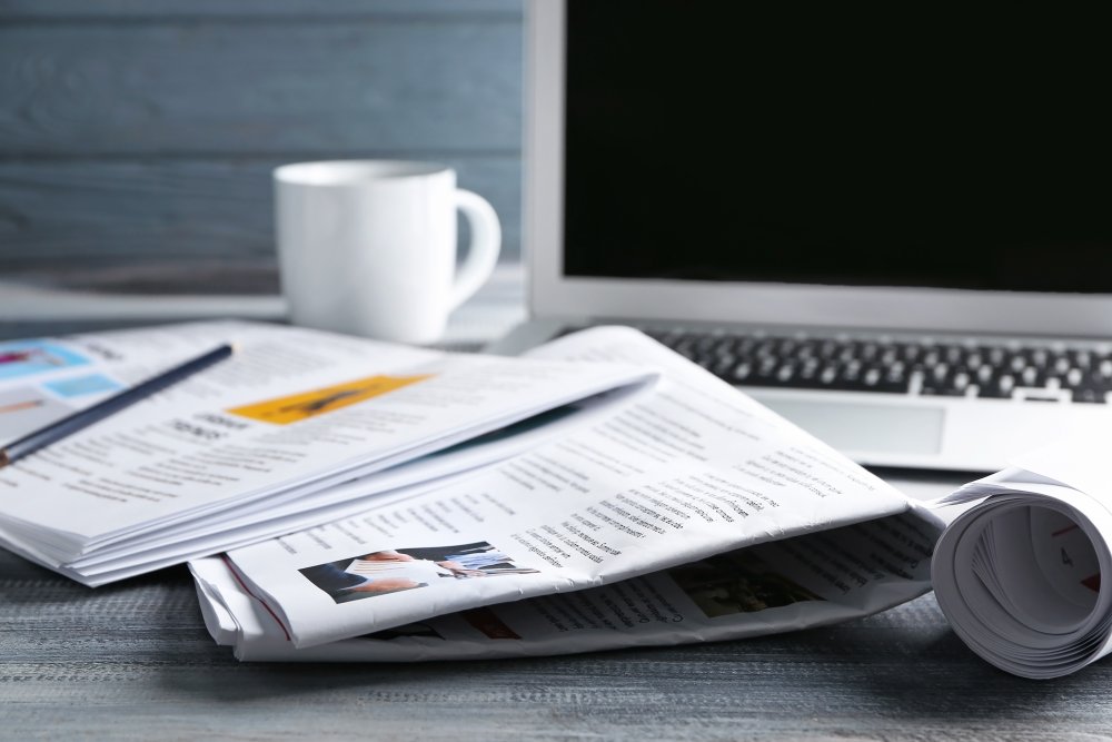 a laptop with a newspaper, magazine and cup of coffee