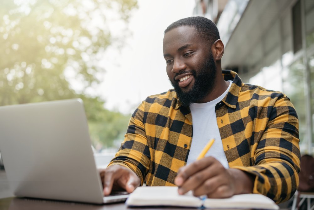 African American man looking at laptop and writing in book 