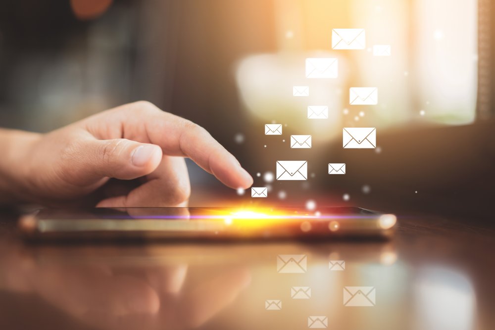 Woman hand using smart phone on old wood table texture background at coffee shop with email icon flying abstract.